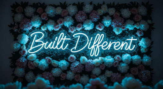 Built Different neon sign in ice blue on flower wall